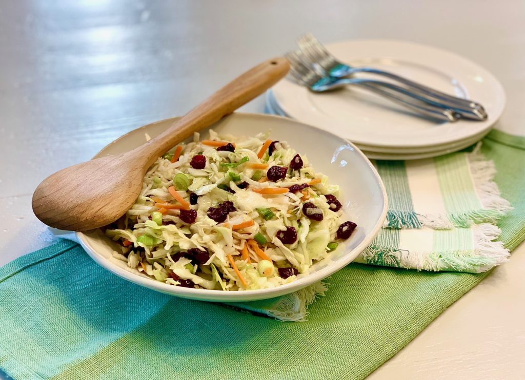 Apple Cider Coleslaw in a bowl with a wooden spoon