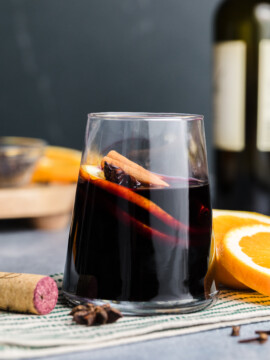 Close-up of mulled wine in a glass with a cinnamon stick and orange peel garnish.