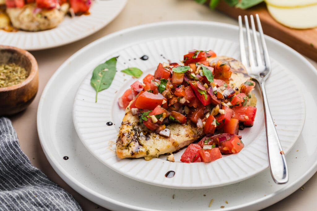 A plate of grilled chicken breast topped with fresh tomato bruschetta, chopped onions, basil, and a drizzle of balsamic glaze, reminiscent of the vibrant flavors found in a Classic Cobb Salad with Blue Cheese Dressing.