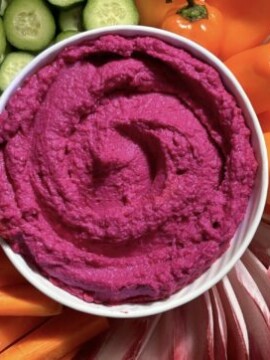 Photo of a bowl of Beet Hummus surrounded by veggies