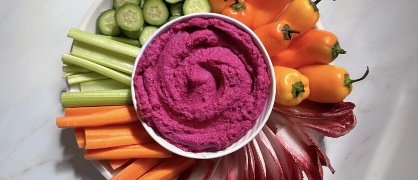 Photo of a bowl of Beet Hummus surrounded by veggies
