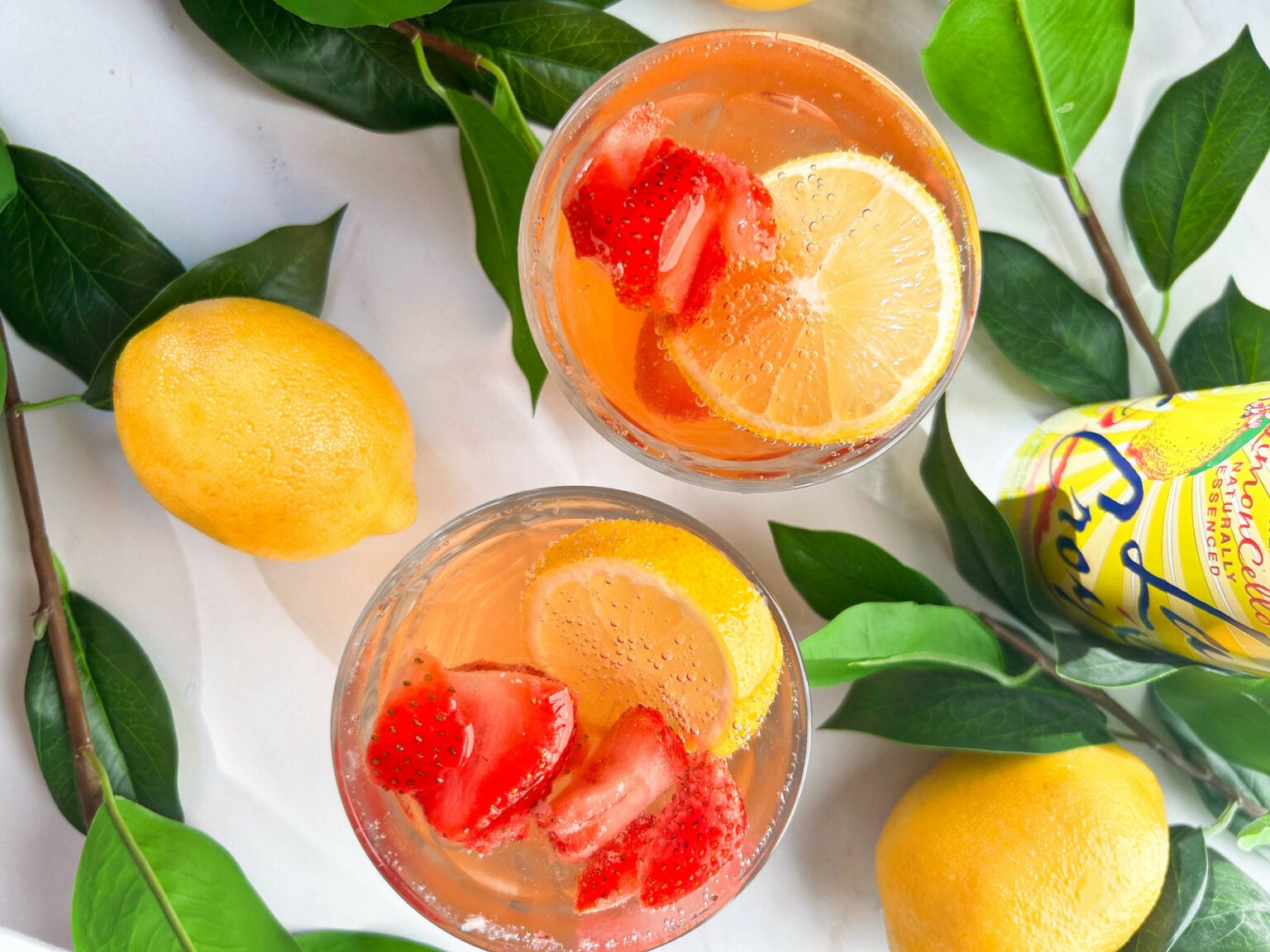 Classic lemonade pitcher with strawberry and blueberry ice cubes melting in glasses for 4th of July patriotic mocktail