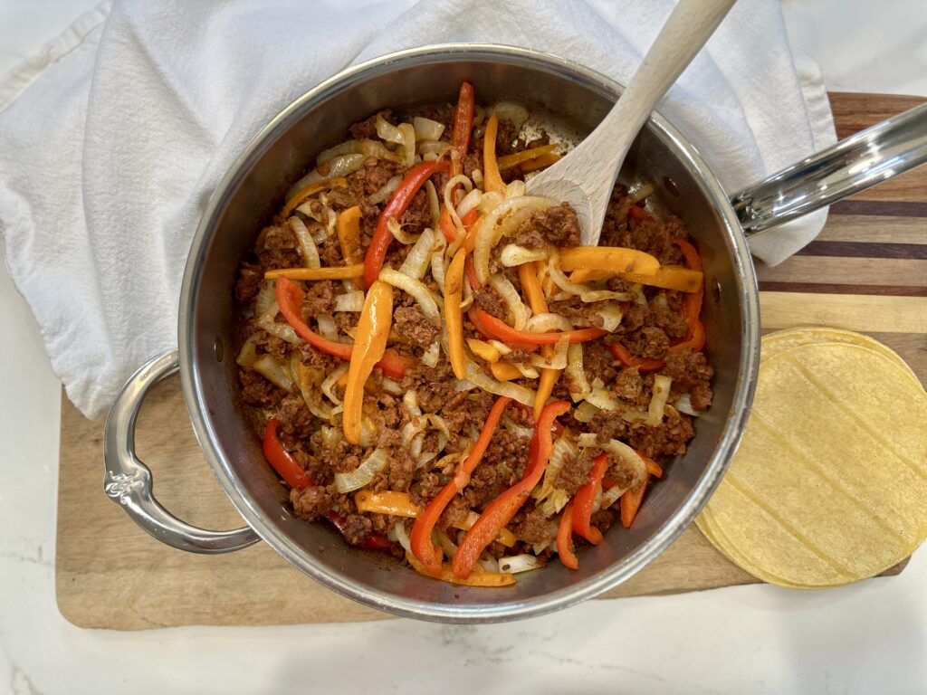 Plant-based Steak, Peppers, and Onions
 in a stainless steel cooking pan