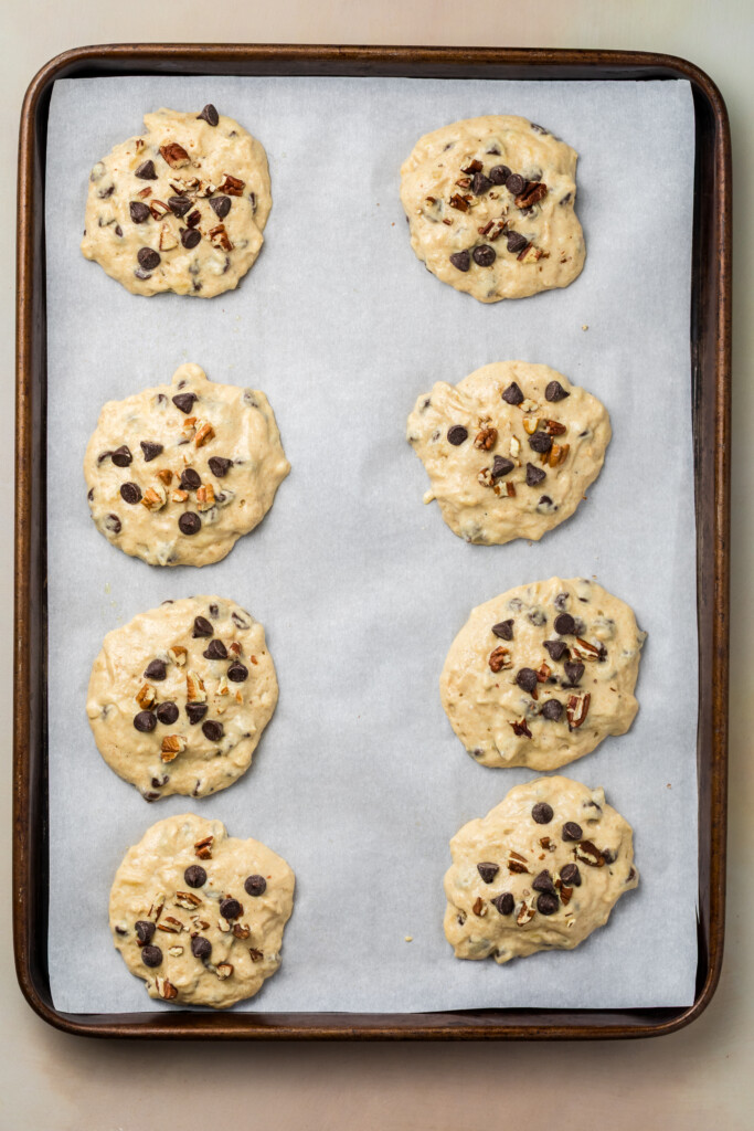 Scoops of banana chocolate chip protein pastry dough arranged on a parchment-lined baking sheet.