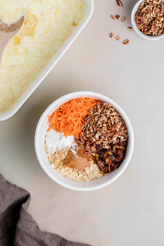 Bowl filled with oats, shredded carrots, pecans, spices, and baking ingredients for carrot cake baked oatmeal.