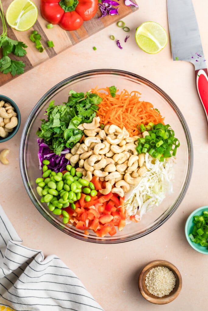 Bowl of edamame crunch salad ingredients including shredded cabbage, carrots, edamame, cashews, and scallions.