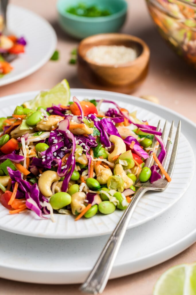 Side-angle view of edamame crunch salad served on a white plate with lime wedge and sesame seeds.