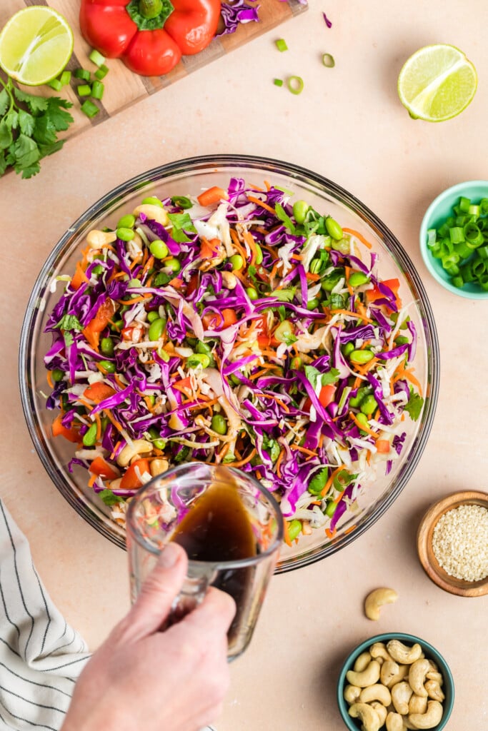 Sesame ginger dressing being poured over a bowl of edamame crunch salad before tossing.