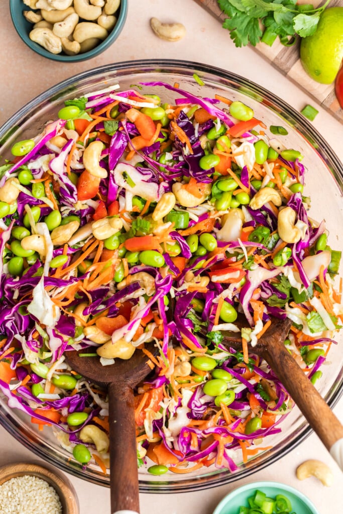 Edamame crunch salad tossed in a large glass bowl with shredded cabbage, carrots, edamame, and cashews.