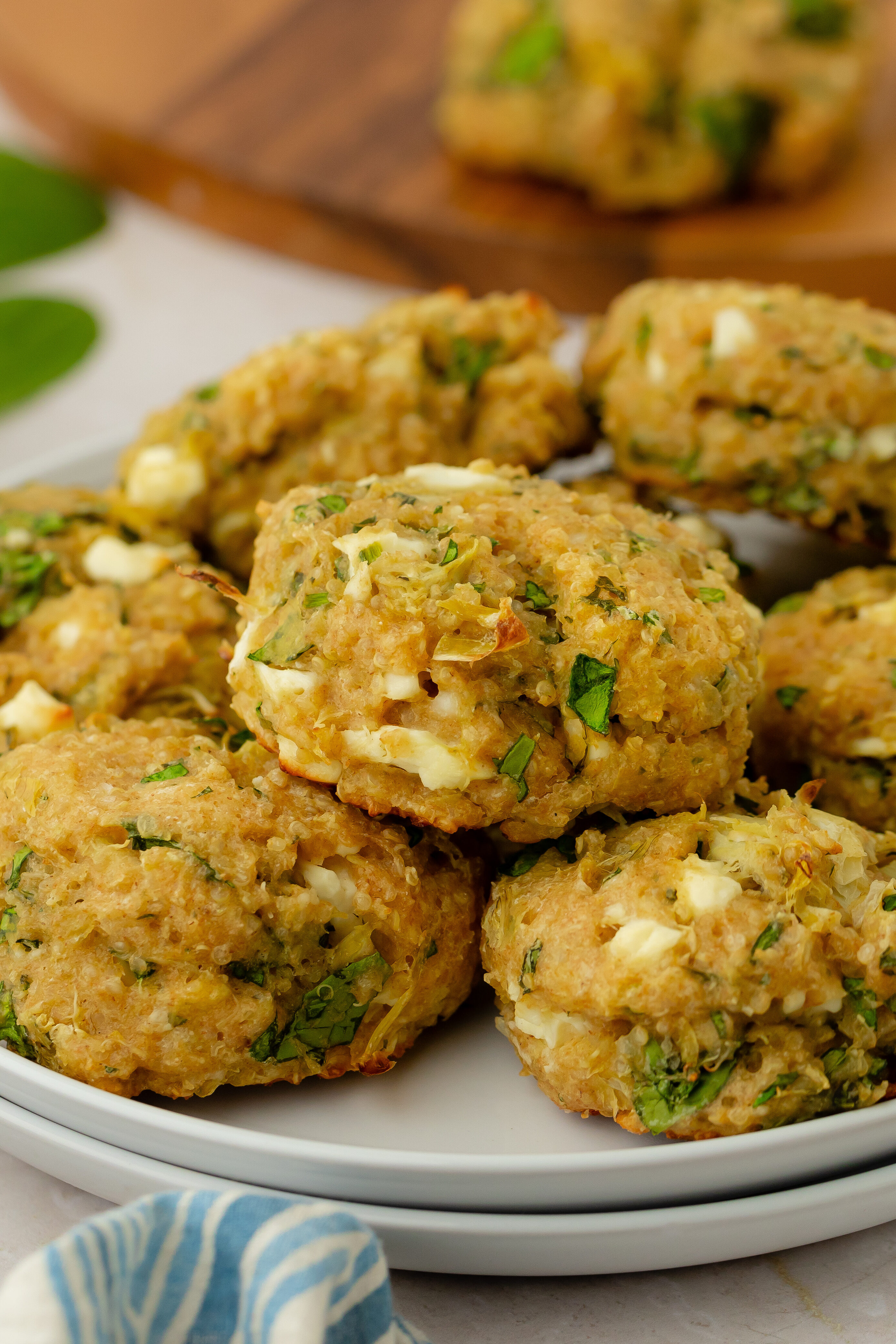 A plate of golden-brown, homemade spinach and cheese patties garnished with herbs, sits on a light countertop beside a bowl of fresh spinach and a blue patterned cloth.