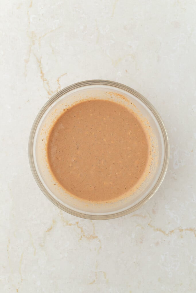 A small glass bowl filled with a light brown, creamy sauce sits on a white marble surface, reminiscent of the rich flavors found in Chocolate Peanut Butter Overnight Oats.