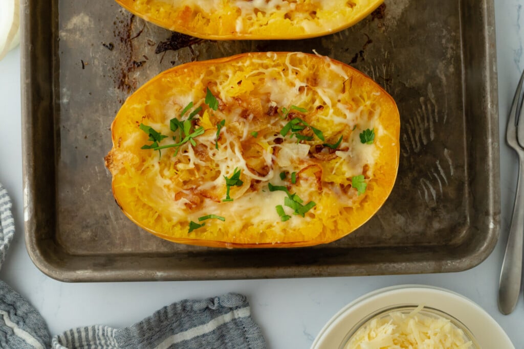 Baked spaghetti squash halves topped with melted cheese and fresh herbs, perfect for healthy fall recipes, on a baking sheet.