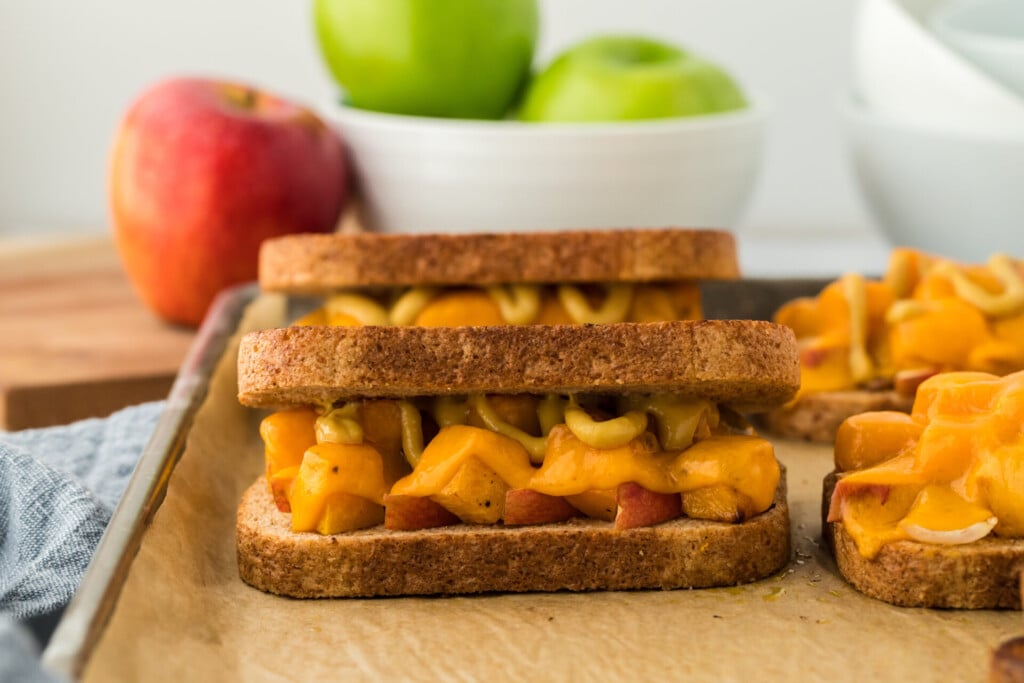 Two apple and melted cheese grilled sandwiches on a baking sheet, with whole apples in the background for a healthy fall recipe.