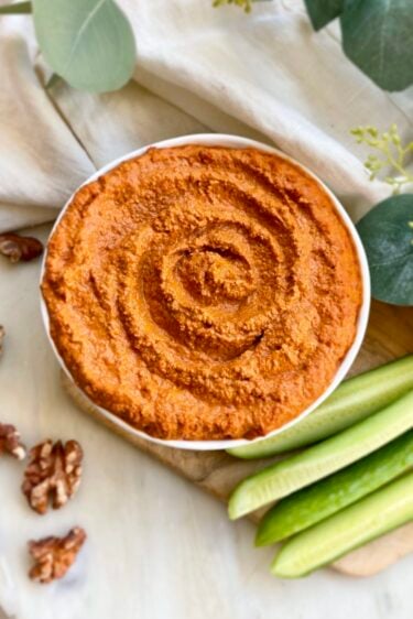 A bowl of roasted red pepper-walnut dip served with cucumber slices.