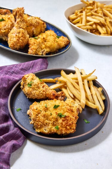 Breaded fried chicken pieces and a serving of french fries on a dark plate, styled similarly to recipes to lower blood pressure, with more chicken and fries in the background.