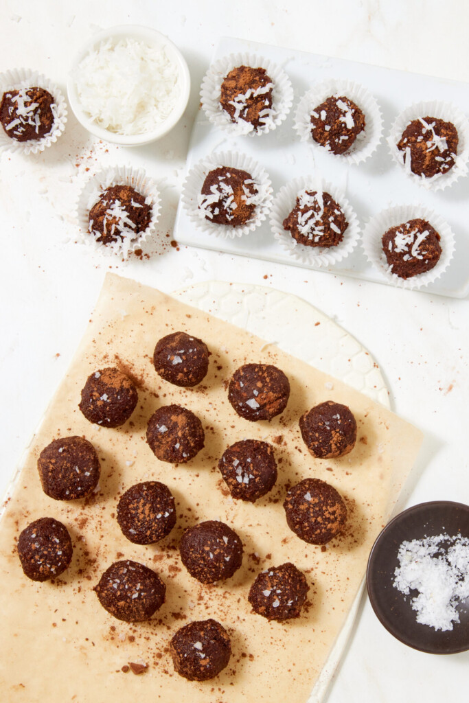 Chewy chocolate caramel candies made with dates, sprinkled with sea salt and shredded coconut, arranged on parchment paper and in paper liners.