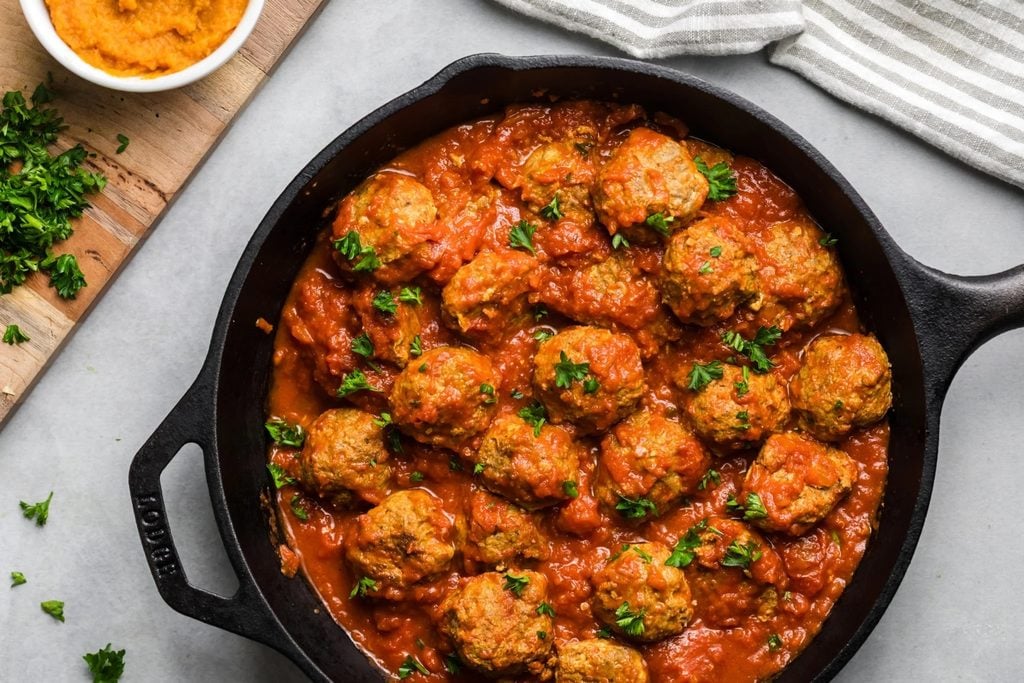 Meatballs simmered in tomato sauce in a black cast iron skillet, garnished with fresh parsley for a healthy fall recipe.